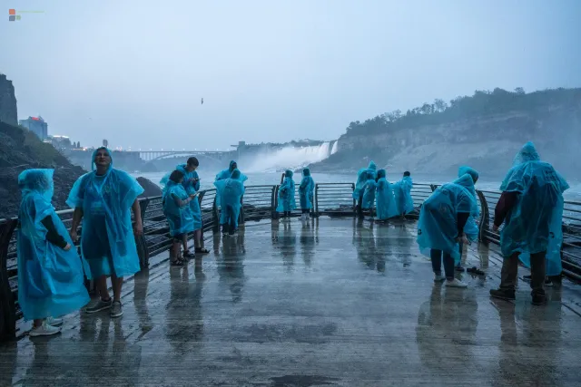 Farblich beleuchteter TunnelMenschen in blauen Plastikponchos trotzen der Gischt auf der Plattform.