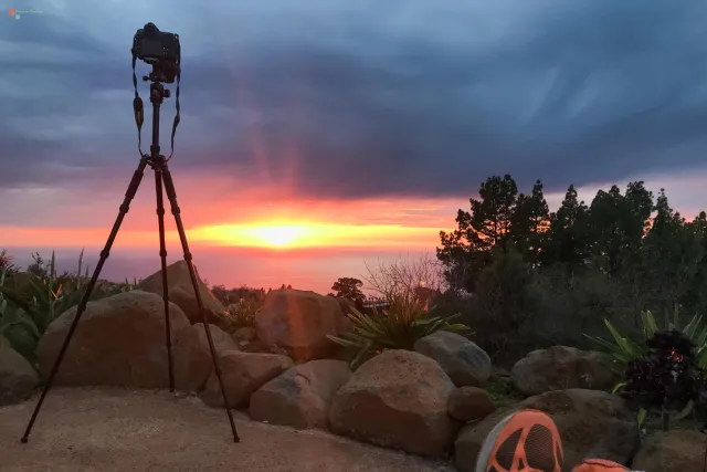 Kamera auf Stativ fotografiert Sonnenuntergang über Wolkenmeer auf La Palma; unten rechts sind die Schuhe des Fotografen zu sehen.